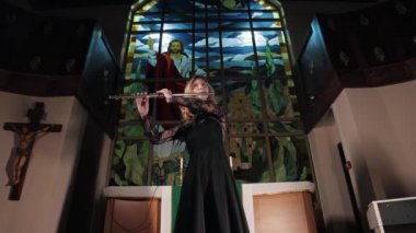 Female flutist playing in church against the background of Christian stained glass windows
