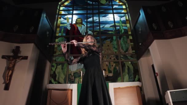 Flautista femenina tocando en la iglesia contra el fondo de vidrieras cristianas — Vídeos de Stock