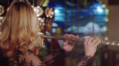 Blonde woman playing flute on a background of stained glass windows