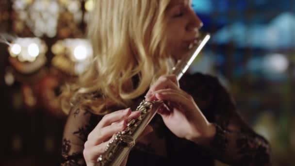 Взрослая блондинка играет на флейте на фоне витражей — стоковое видео