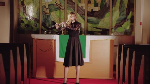 Woman flutist playing in church against the background of stained glass windows — Stok Video