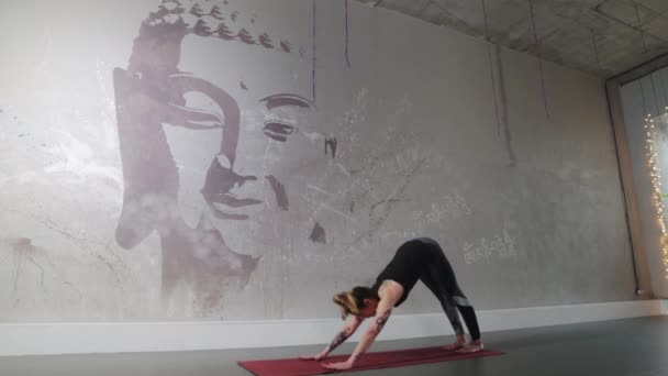 Una mujer con tatuajes se dedica a la aeróbic sobre el fondo de una pared con la imagen de un buda — Vídeos de Stock