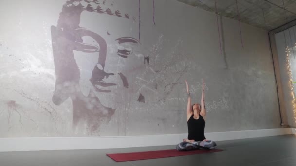 Mulher de plástico com tatuagens meditando contra o fundo de uma parede com a imagem de um Buda — Vídeo de Stock