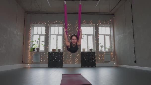 Повітряна йога - молода жінка накладає своє тіло на гамак і гойдається — стокове відео