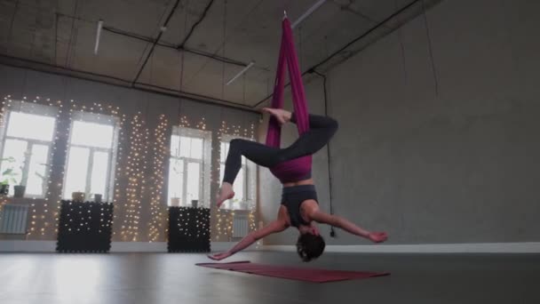 Aerial yoga - a young woman hanging in a hammock with her head upside down — Stock video