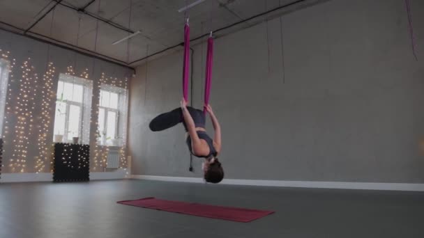 Повітряна йога - молода жінка, що звисає догори ногами в рожевому гамаку — стокове відео