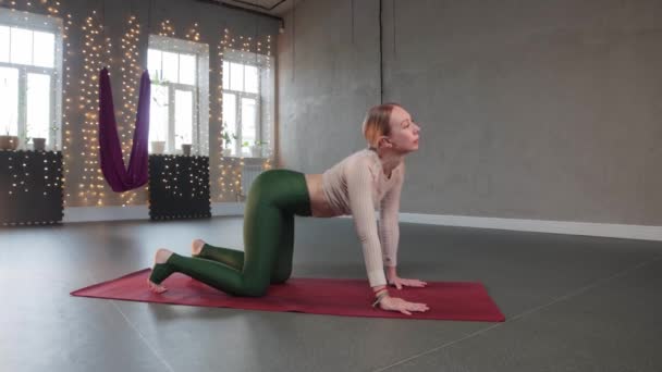 Yoga aéreo - uma mulher flexionando as costas e o corpo em um tapete de ioga — Vídeo de Stock