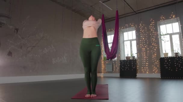 Йога в помещении - женщина в студии растягивает спину стоя на коврике для йоги — стоковое видео