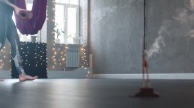 Stüdyoda tütsü yakan bir kadın yere yoga minderi seriyor.