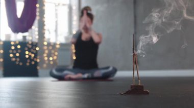 Stüdyoda yanan tütsü. Arka planda meditasyon yapan bir kadın.