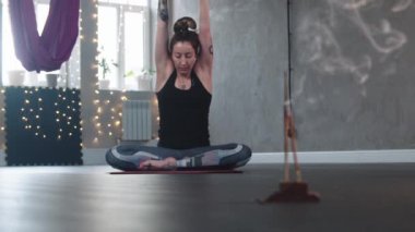Stüdyoda tütsü yakan bir kadın yoga minderinde oturur ve vücudunu gerer.