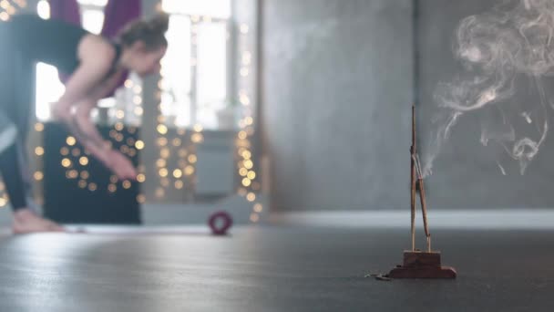 Тлеющий ладан в студии - женщина расстилает коврик для йоги на полу и стоит в позе — стоковое видео