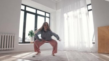 Modern dans. Uzun saçlı genç bir kadın. Telefonundan müzik eşliğinde dans ediyor.