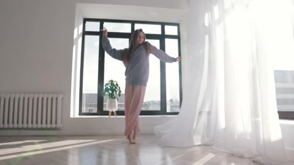 Сучасні танці - молода жінка в блакитному светрі танцює у просторій кімнаті біля вікон — стокове відео