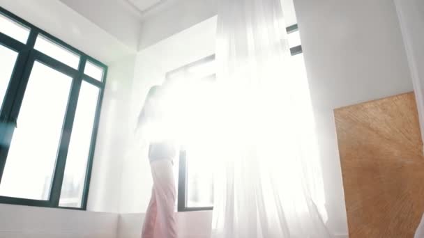 Молода жінка танцює перед вікном у світлому денному світлі — стокове відео