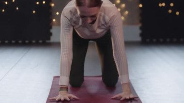 Sarışın kadın yoga minderinde sırtını esnetiyor.