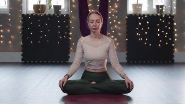 Bir kadın yoga minderine oturur ve nefes egzersizleri yapar.