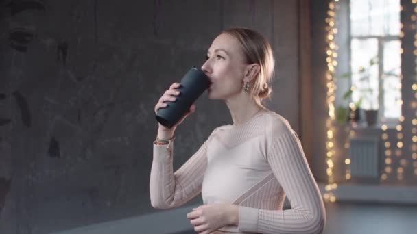 Жінка в білому светрі п'є воду в студії — стокове відео