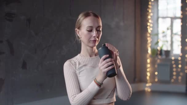 Фітнес жінка в білому светрі п'є воду в студії — стокове відео