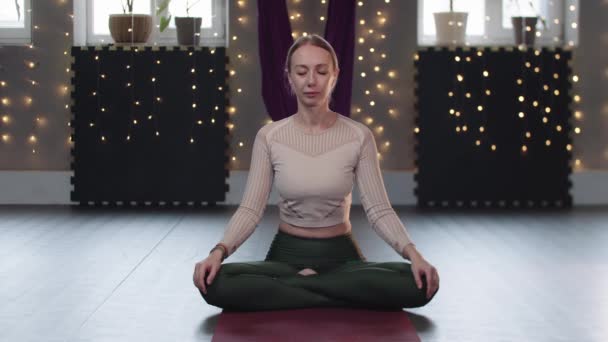 Uma mulher senta-se em um tapete de ioga e faz exercícios de respiração — Vídeo de Stock