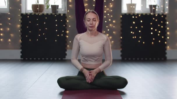Блондинка сидить на килимку для йоги і виконує дихальні вправи — стокове відео