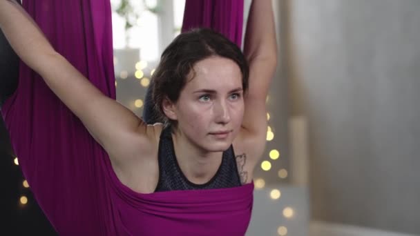 Jovem mulher pendurada na rede de ioga roxa e segurando seus tornozelos — Vídeo de Stock