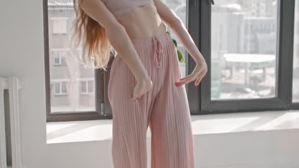 A plastic young woman in pink pants dancing in a bright apartment — Stock Video