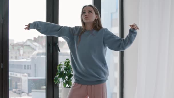 Молодая женщина в синем свитере чувствует музыку в яркой квартире — стоковое видео