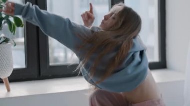 Genç bir kadın dans ediyor ve mavi kazağını çıkarıyor.