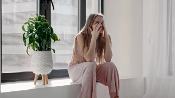 Una giovane donna triste siede sul davanzale e si aggrappa alla testa — Video Stock