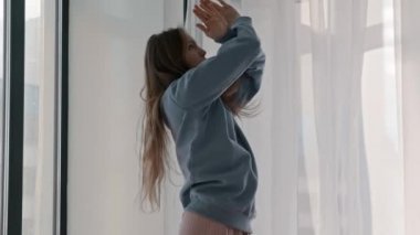 Pastel elbiseli genç kadın pencere kenarında modern dans gösterisi yapıyor.