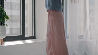 Pastel elbiseli, genç, güzel bir kadın. Pencere kenarında dans ediyor.