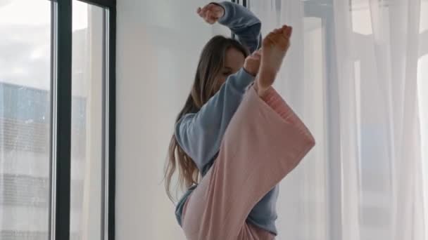 Молодая женщина в пастельной одежде чувствует музыку у окна — стоковое видео