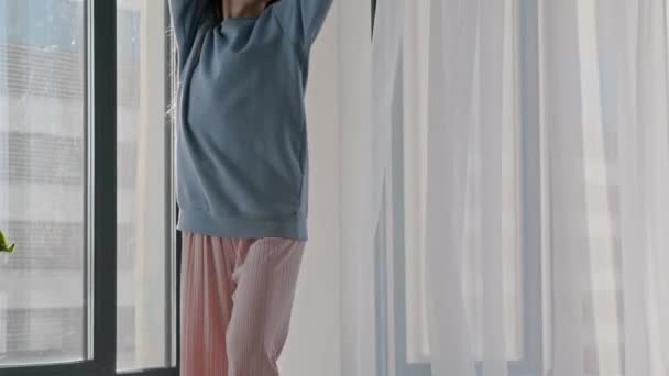 Молода жінка в пастельному одязі танцює біля вікна — стокове відео