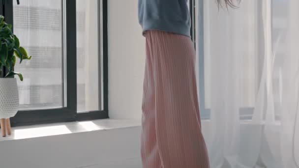 Νεαρή όμορφη γυναίκα με παστέλ ρούχα που χορεύει δίπλα στο παράθυρο — Αρχείο Βίντεο