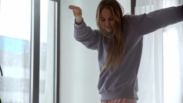 Młoda kobieta z długimi włosami tańcząca przy oknie w dzień — Wideo stockowe