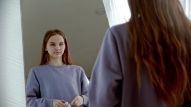 Genç bir kadın aynaya doğru yürür ve kablosuz kulaklıklarını takar.