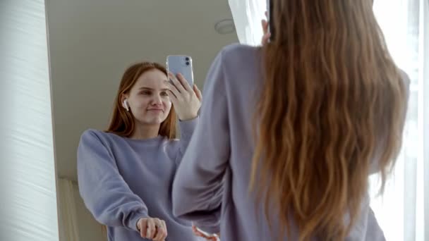 A young woman dancer in wireless headphones shoots herself in the mirror — Stock Video