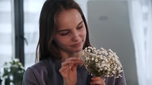 Młoda kobieta trzyma małe białe kwiaty i patrzy w kamerę. — Wideo stockowe
