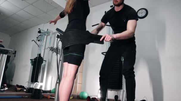 Un coach homme habille une femme dans un costume de fitness EMS dans la salle de gym — Video