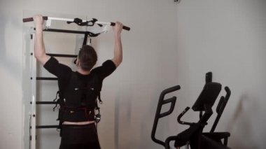 Elektro uyarıcı ekipmanlı yelek giyen bir adam barfiks çekiyor ve kordonu çözüyor.