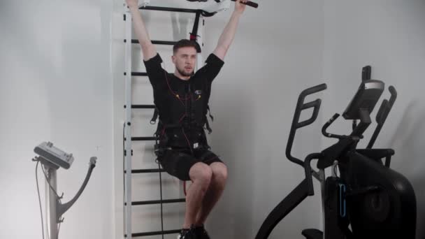 Homme concentré portant un équipement d'électro-stimulation accroché au stand et pompant ses muscles du bas de l'estomac — Video