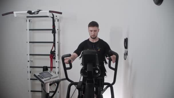 Ein Mann mit Elektrostimulationsanzug und Training auf dem Heimtrainer — Stockvideo