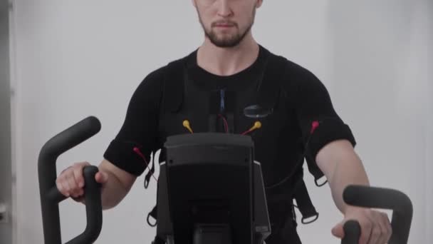 Tampan pria mengenakan jas elektro-stimulasi dan pelatihan pada sepeda olahraga — Stok Video