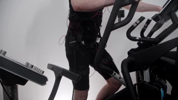 Bearded man in ems suit turns on the electric stimulation and starts working out on exercise bike — Stock Video