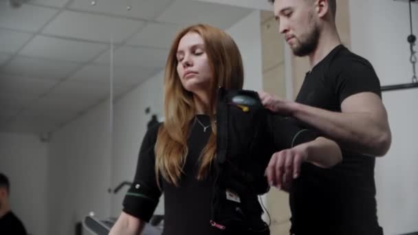 Un homme habille jeune femme en costume de fitness de stimulation électrique — Video