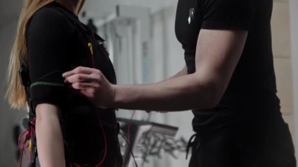 Een man kleedt zich jong vrouw in elektrische stimulatie fitness pak en hecht de draden aan het — Stockvideo