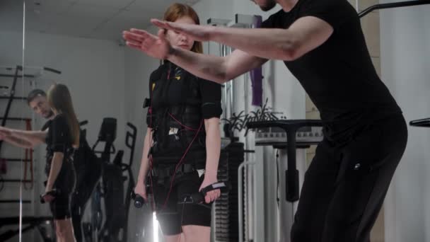 Чоловік, який пояснює вправи молодій жінці в костюмі EMS — стокове відео