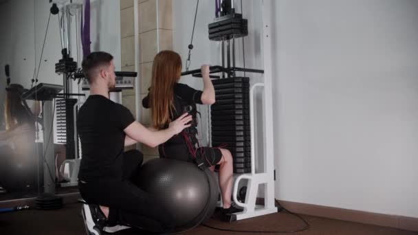 Férfi edző segít a fiatal nő egy EMS jelmez képzés tornaterem — Stock videók
