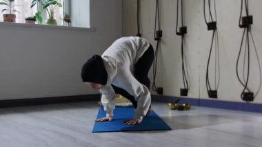 Tesettürlü bir kadın yoga minderinde yoga yapıyor ve ellerine yaslanıyor.